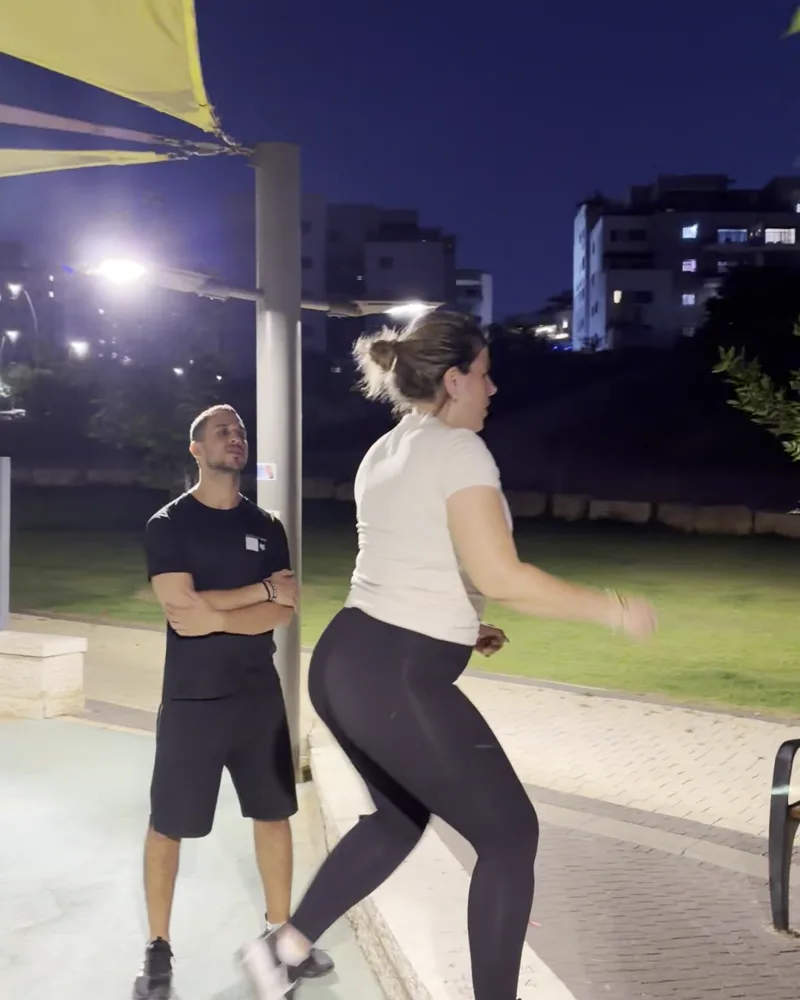 מתאמנת מקבוצת האמהות בתרגיל מדרגה, עם המאמן לצידה