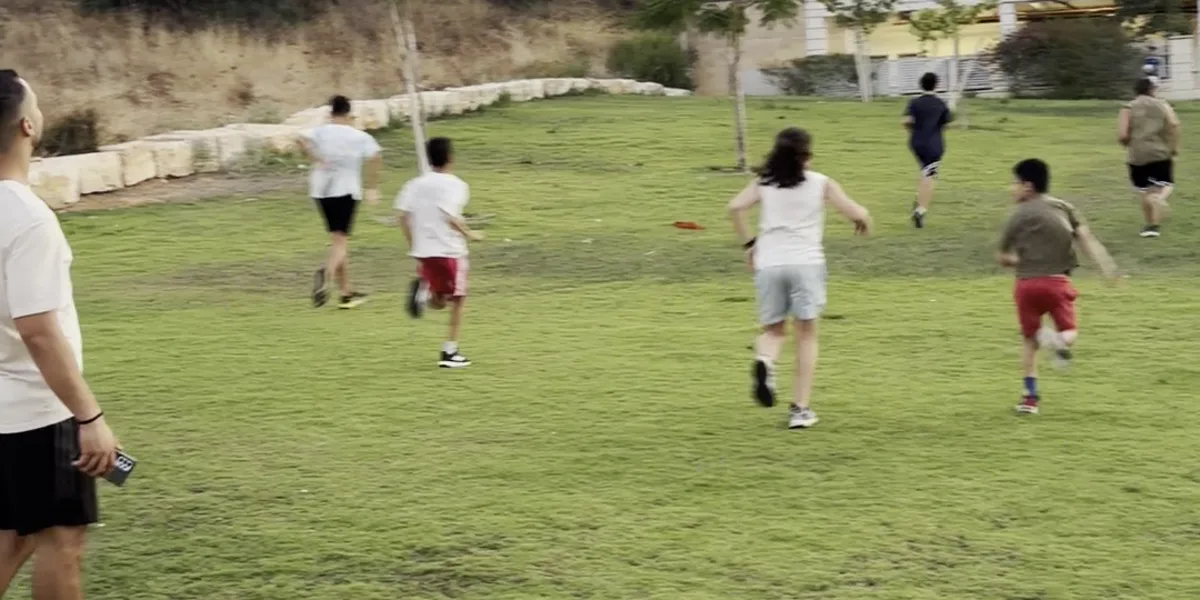 קבוצת הילדים של טים לידר רצה על הדשא באימון אחר הצהריים, המאמן מלווה מהצד