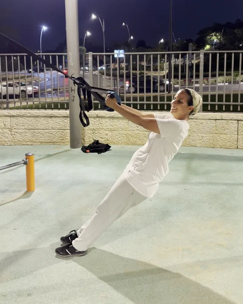 מתאמנת מקבוצת האמהות בתרגיל TRX בגינת הכושר בפסגות אפק, בשעת ערב